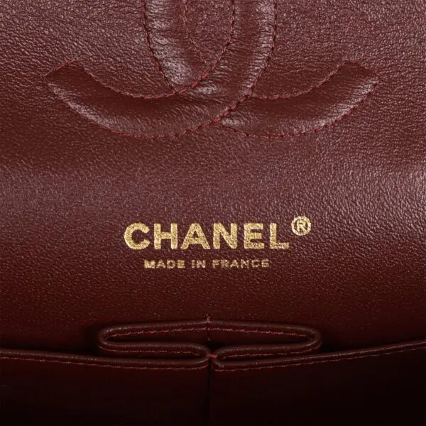 The Chanel Medium Classic Double Flap Bag Black Caviar Gold Hardware logo on a burgundy leather bag.