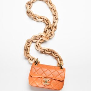 An orange MINI FLAP BAG on a chain.