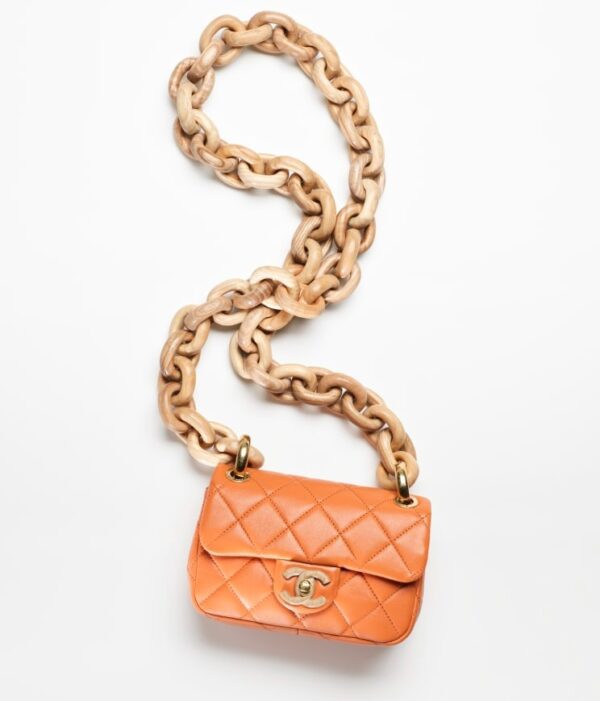 An orange MINI FLAP BAG on a chain.